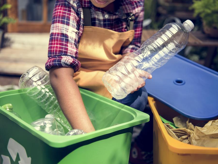 A young person places plastic bottles in a recycling bin